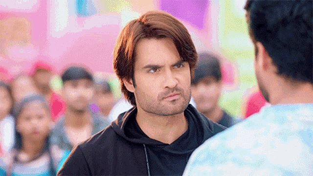 a man in a black hoodie is looking at another man in a blue shirt