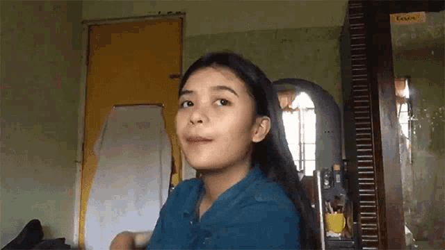 a girl in a blue shirt is standing in front of a mirror in a room with a yellow door