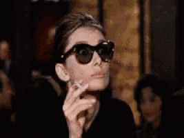 a woman wearing sunglasses is smoking a cigarette in a restaurant .