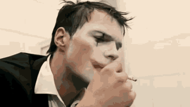 a man with clown makeup on his face is smoking a cigarette in a bathroom .