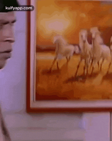 a man is standing in front of a painting of horses and looking at it .