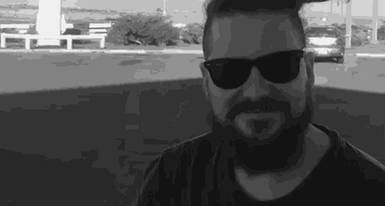 a black and white photo of a man with a beard wearing sunglasses and smiling .
