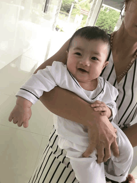 a woman is holding a baby in her arms and the baby is smiling for the camera