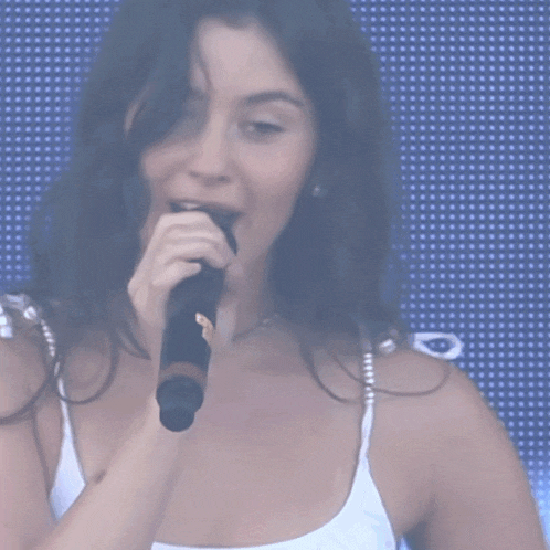 a woman in a white tank top is holding a microphone