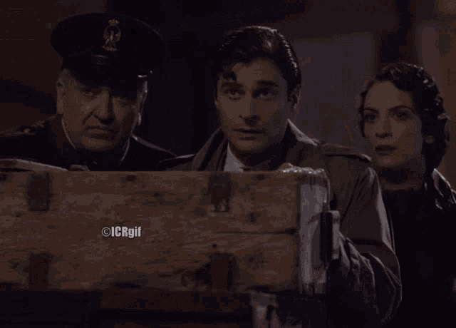 a man in a military uniform stands between two women and a man in a suit behind a wooden box