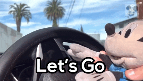 a stuffed mickey mouse is driving a car with the words let 's go on the steering wheel