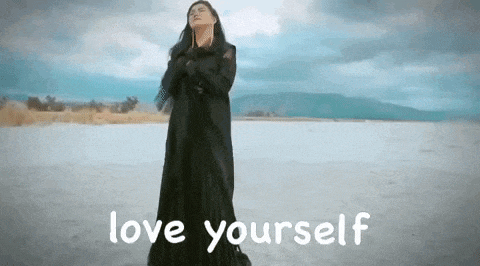 a woman in a long black dress is standing on a beach with the words `` love yourself '' written on the bottom .