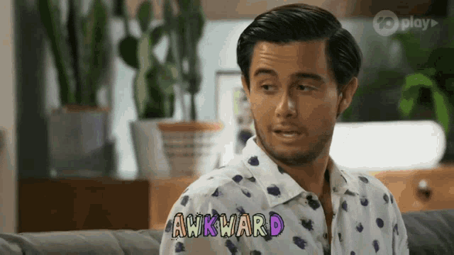 a man is sitting on a couch with the word awkward written on his shirt