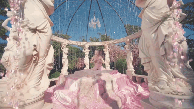 a statue of a woman laying on a bed with pink petals
