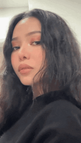 a woman with long dark hair is wearing a black shirt and looking at the camera