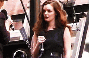 a woman in a black dress is holding a microphone and talking to someone .