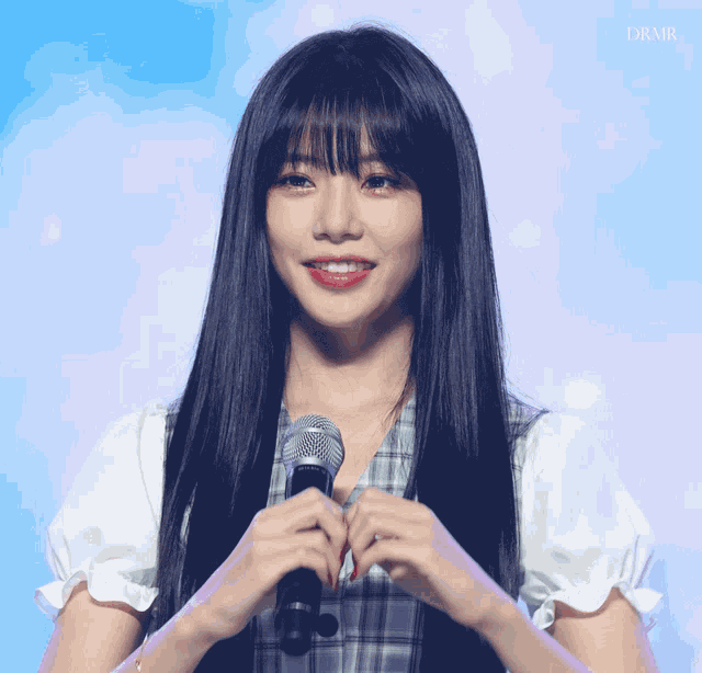 a woman with long black hair and bangs holds a microphone in her hand