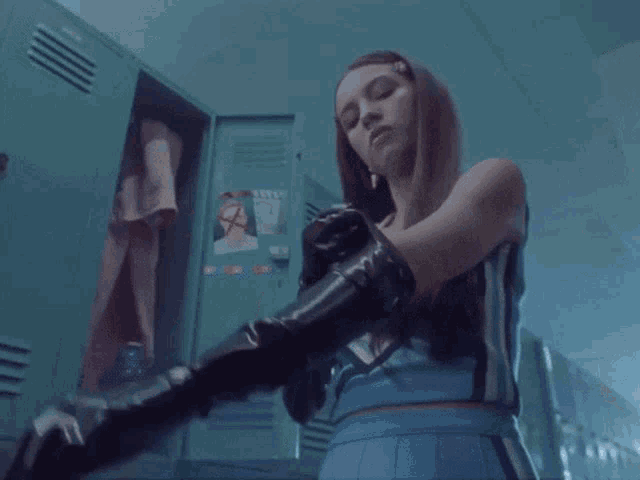 a woman wearing black gloves is standing in front of a locker with a sticker on it that says no smoking