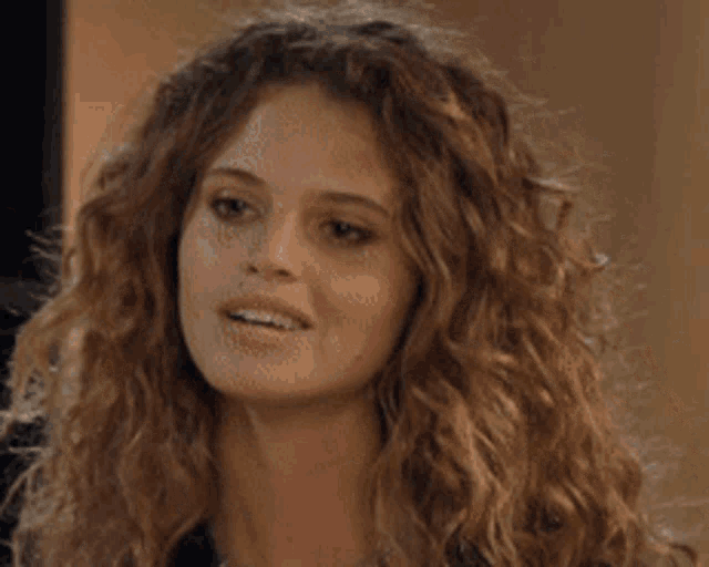 a woman with curly hair is smiling and wearing a necklace