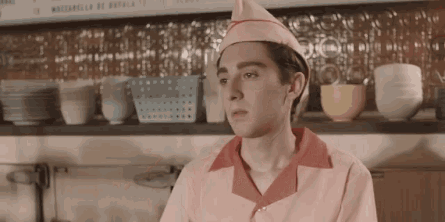 a man in a pink uniform stands in front of a shelf with bowls