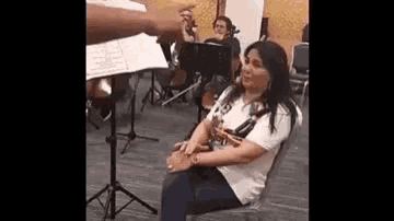 a woman is sitting in a chair in front of an orchestra while a man plays a flute .