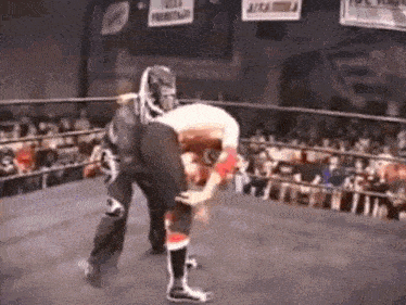 a wrestler is carrying another wrestler on his back in a wrestling ring .