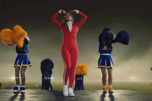a cheerleader in a red jumpsuit is surrounded by cheerleaders in blue and yellow uniforms
