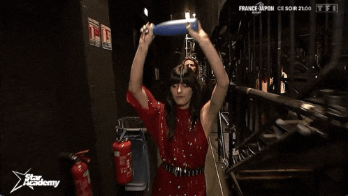 a woman in a red dress is holding a frisbee in front of a fire extinguisher that says " star academy "