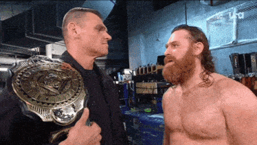 two men are standing next to each other and one has a championship belt on his chest