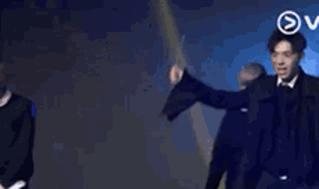 a man in a black coat is standing on a stage with a microphone .