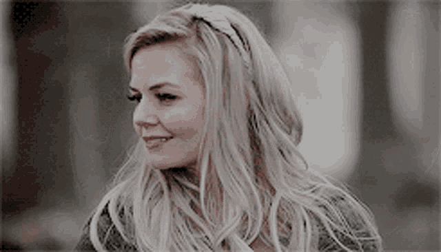 a woman with long blonde hair is smiling and wearing a gray sweater .