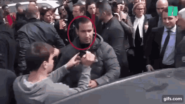 a man is talking to another man in a crowd of people while another man takes a picture of him .