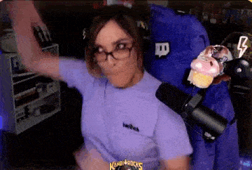 a woman wearing glasses and a purple shirt is standing in front of a microphone in a room .