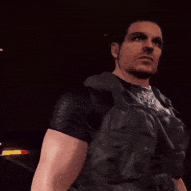 a man in a black vest stands in a dark room with his eyes closed