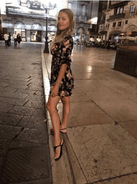 a woman in a floral dress is standing on a sidewalk in front of a billboard for toyota