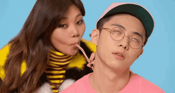 a woman is drinking from a straw next to a man with glasses