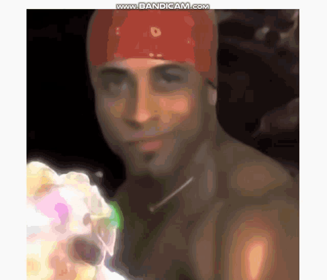 a shirtless man wearing a red bandana is holding a cake in his hand .