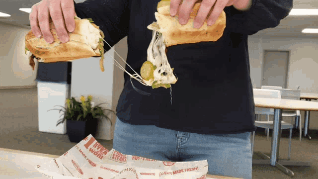 a man is holding a sandwich with cheese pulled out of it that says ' steaks made fresh ' on it