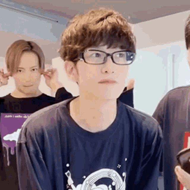 a young man wearing glasses and a black t-shirt is standing next to another young man .