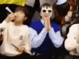 a group of people are sitting in a row and one of them is wearing a mask with the word birthday on it .