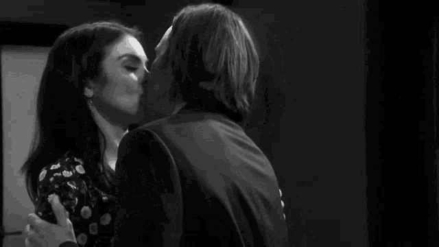 a black and white photo of a man and woman kissing .
