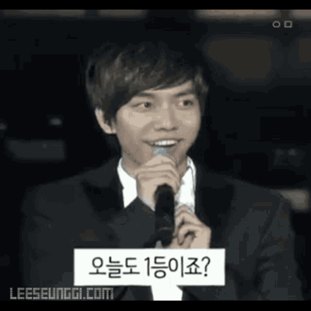 a man in a suit is holding a microphone with a sign that says leeseunggi.com