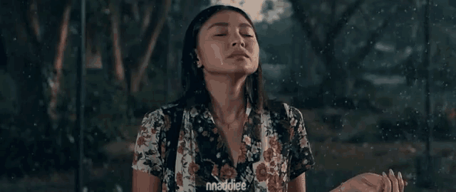 a woman in a floral shirt is standing in the rain with her eyes closed and her hands in the air .