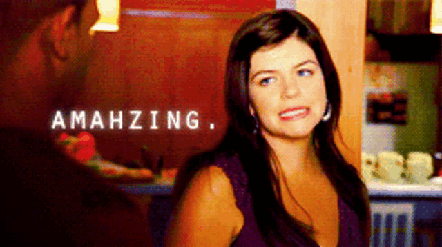 a woman in a purple top is standing in front of a wall that says amahzing on it
