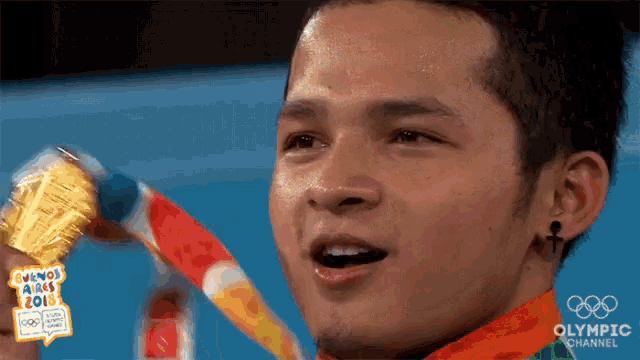 a man is holding a gold medal with the olympic channel written on the bottom