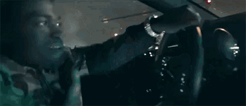 a man is driving a car at night and smoking a cigarette while another man looks on .