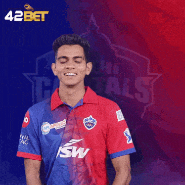 a man wearing a delhi capitals shirt stands in front of a blue and red background
