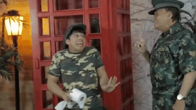 a man in a camo shirt is holding a roll of toilet paper while talking to a man in a military uniform