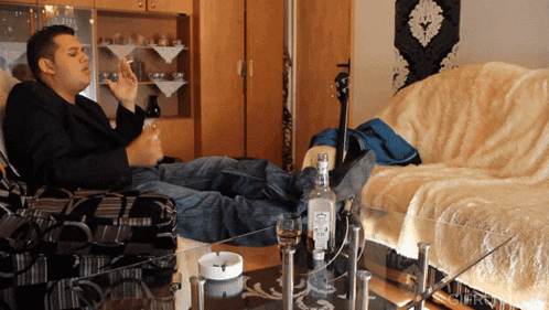 a bottle of jack daniels sits on a glass table next to a man smoking a cigarette