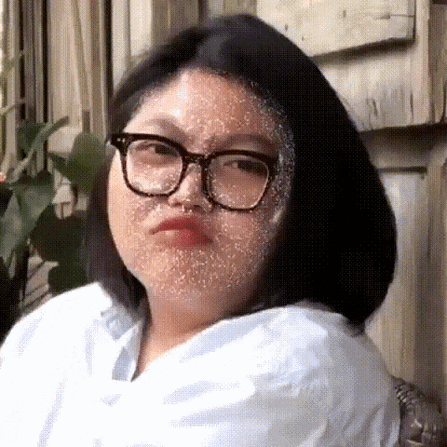a woman wearing glasses and a white shirt making a funny face .