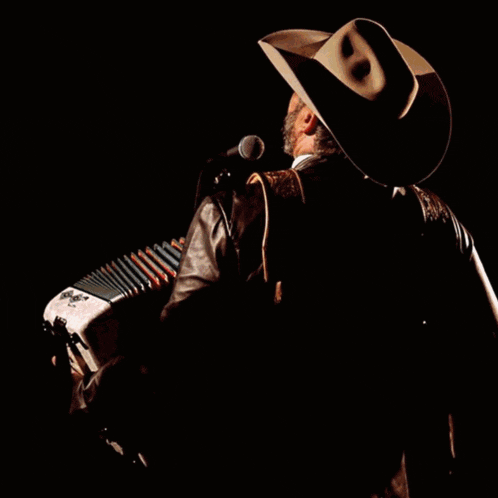 a man in a cowboy hat is singing into a microphone while playing an accordion