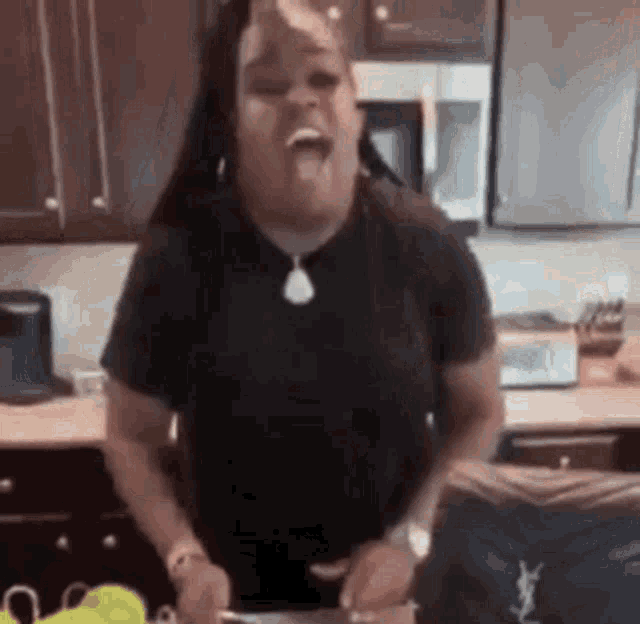 a woman is standing in a kitchen cutting vegetables and making a funny face .