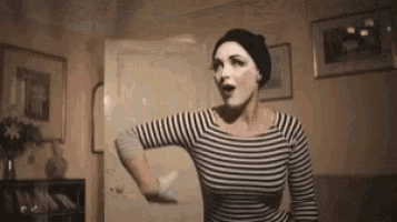 a woman in a striped shirt and a black hat is dancing in a room .