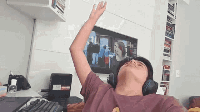 a man wearing headphones is sitting in front of a television with his hand in the air .