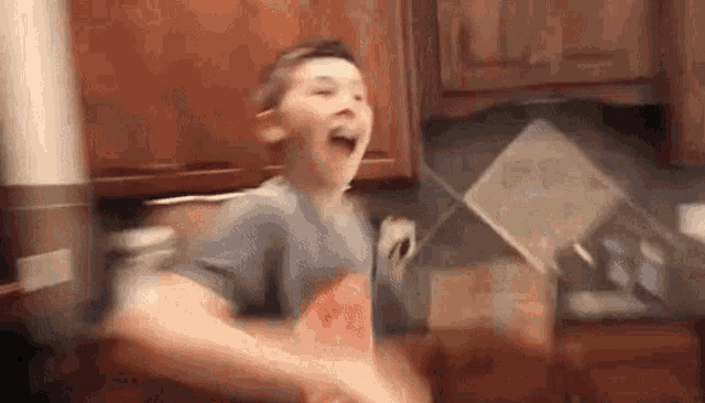 a young boy is standing in a kitchen with his mouth open and holding a bag of chips .